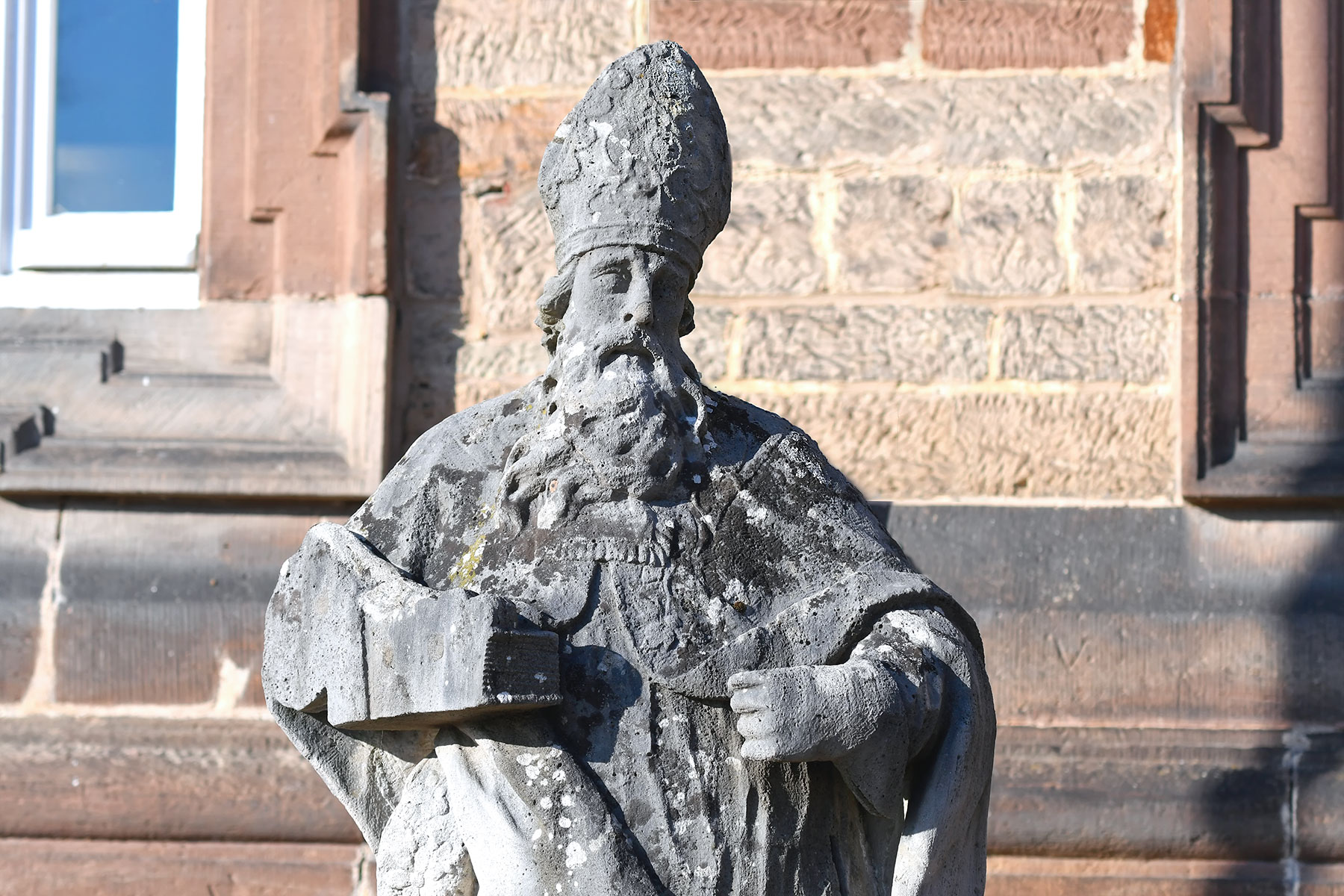 Steinerne Statue eines bärtigen Mannes mit Krone, der ein Reichsapfel-Symbol in der Hand hält, vor einer Sandsteinfassade.