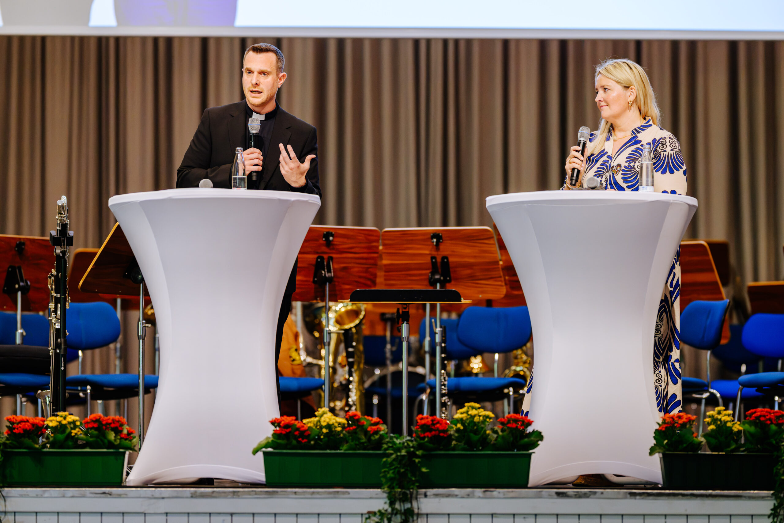 Zwei Personen, ein Mann eine Frau mit einem Mikro vor einem Stehtisch